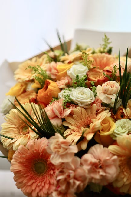 A vibrant floral gift arrangement featuring a mix of peach-pink gerbera daisies, soft orange roses, pale green and white lisianthus, and small clusters of yellow and green filler flowers, all compleme