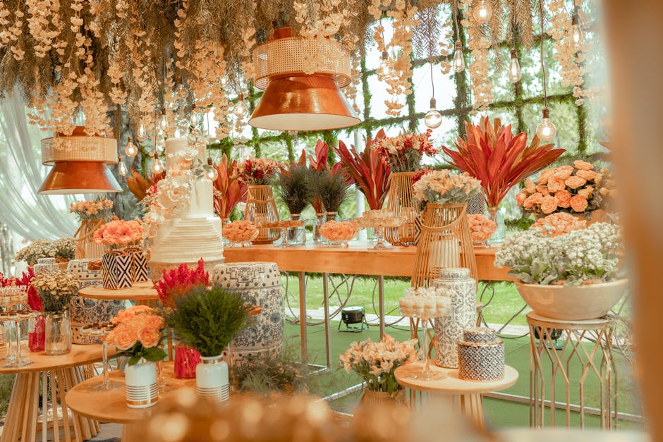 A floral arrangement display featuring a variety of fresh flowers in soft pinks, whites, and deep red hues, including roses, lilies, and chrysanthemums, arranged in elegant vases and baskets across wo